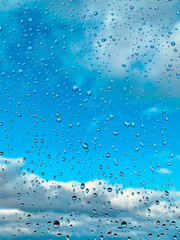Raindrops on a glass with blue sky and clouds.