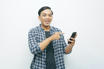 Portrait of young Asian Indonesian smiling while other hand finger pointing to smartphone. Blue flannel shirt casual outfit