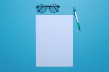 White empty a4 paper mockup, glasses and pen isolated on blue background. Top view, flat lay