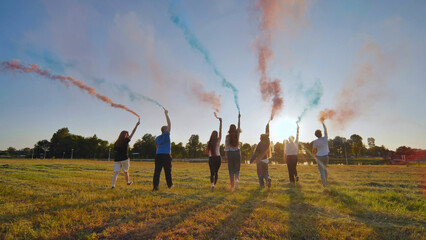 A group of friends spraying multi-colored smoke at sunset. - obrazy, fototapety, plakaty