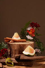 Pomelo and cinnamon are displayed on a wooden platform. Fresh flowers and green leaves are...