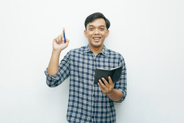 Fototapeta premium Portrait of young Asian Indonesian man smiling when holding small notebook with ballpoint pen with isolated white background