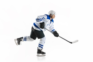 Young man, motivated athlete, hockey player in motion with stick on rink, training against white studio background