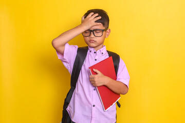 Forgetful Asian boy touching forehead while hold books at school. 