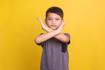 Serious little boy crossing hands and looking at camera with aggression, showing stop gesture over yellow background - obrazy, fototapety, plakaty