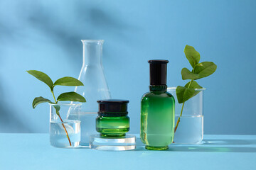 Laboratory concept for advertising cosmetic product with green tea extract. Some lab glassware containing transparent liquid and leaves of green tea on blue background with shadow of natural leaves