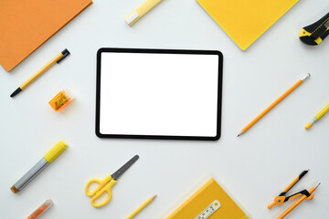 Digital tablet with empty screen surrounded by stationery on white background. Flat lay, top view