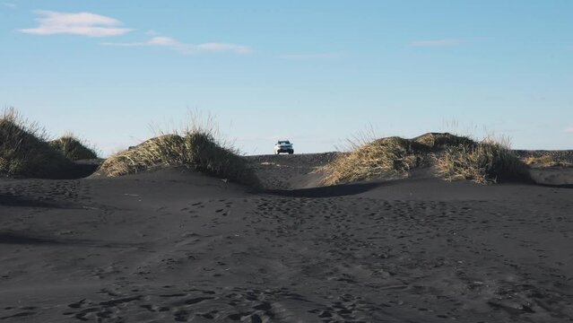 Car parked between two grass turfs on black sand beach in Iceland.