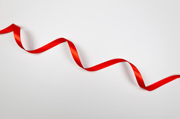 Top view of red ribbon on white background. Shiny rolled fabric, silk and satin material. Copy space. 
