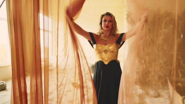 fantasy sexy woman walking in room full sand desert. blonde hair beauty face. fashion model girl in black long dress golden corset warrior armor gold old style. barefoot steps art creative video 4k