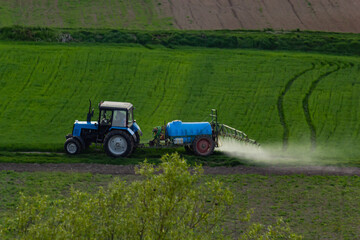 Fototapeta premium Aerial view of tractor spraying crop in green farm fields with pesticide