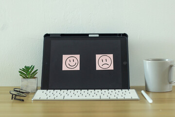 Happy and Sad emoticon sticky notes on laptop screen