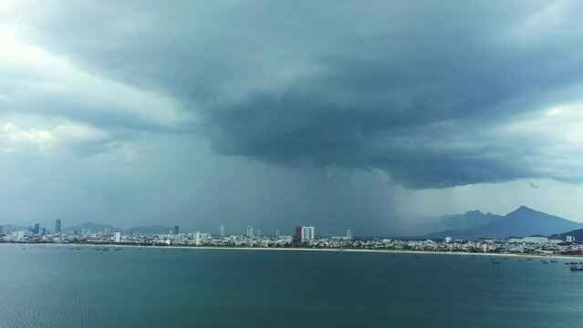 Drone, landscape and rain on city with a cloud, storm or tropical winter weather in town with buildings and cityscape. Vietnam, coast and ocean skyline with dark clouds, water and natural development