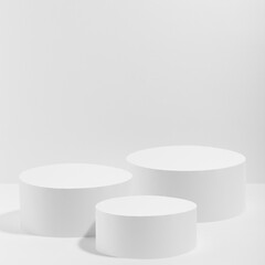 Abstract white stage with three white round podiums mockup for cosmetic products in hard light on white background. Scene for presentation cosmetic products, gifts, goods, advertising, design, sale.