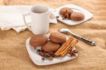 Chocolate cookies, cinnamon, star anise on a ceramic saucer with a cup on a jute cloth.