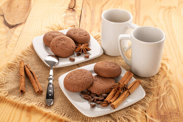 Chocolate cookies, cinnamon, star anise, coffee beans on a ceramic plate with a cup on a wooden table.
