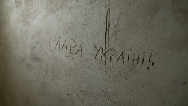 "Glory to Ukraine" is scratched on  concrete wall of the bomb shelter
shelter of civilian population in Ukraine during the war
close-up of the "Slava Ukraini" inscription on the wall
patriotic words