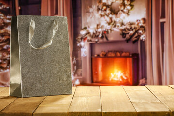 Gift bag on wooden table and free space for your decoration. Home interior with fireplace and window. 