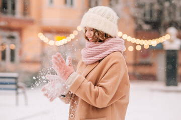 A young beautiful woman shakes snow off her knitted mittens against the backdrop of a winter...