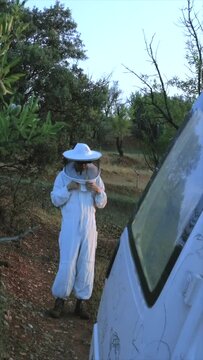 A beekeeper dress up close to the van in the forest