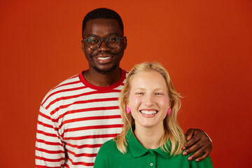 Portrait of happy multiracial couple cuddling and smiling at camera isolated on orange background