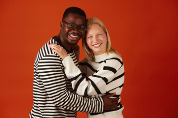 Portrait of happy multiracial couple cuddling and smiling at camera isolated on orange background