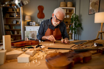 Senior carpenter craftsman carving wood and making violin instrument