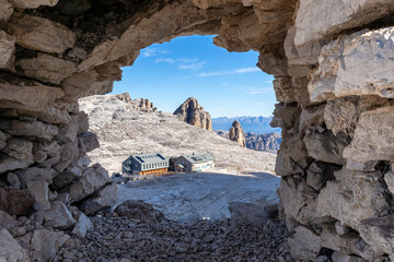 View of the rifugio Boe mountain hut through a stone window in the cairn. Dolomites, Italian Alps. Sella massif
