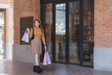 Beautiful Asian woman holding shopping bags and smiling while shopping on Black Friday outside the mall