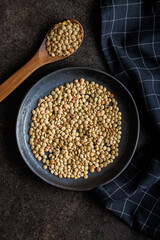 Uncooked lentil legumes on plate on black table. Top view.