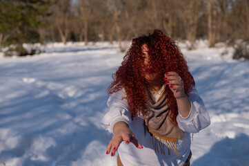 The plump-cheeked woman threw her red hair over her face and held out her arms like a zombie. Girl fooling around in the park in winter. 