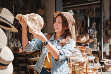 Asian tourist girl shopping, walking in famous local street market looking at beautiful straw hats,...