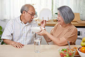 senior woman feeding rice porridge to senior man in the kitchen