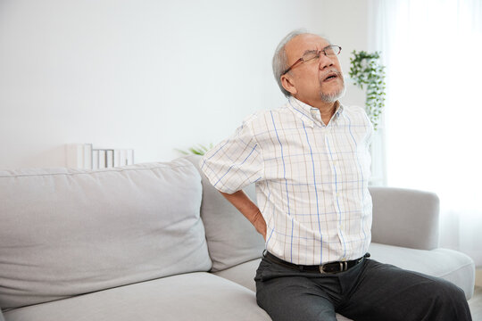 senior man suffering from back pain on sofa - Powered by Adobe