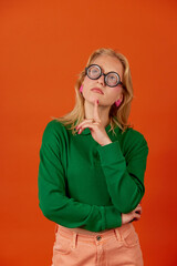 Woman standing with thoughtful serious smart expression against orange background