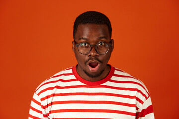 Shocked or surprised African-American man with open mouth on orange background