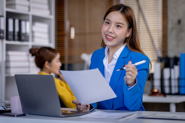 Young Asian business woman office worker analyst sitting at desk working on laptop thinking on project plan, analyzing marketing or financial data online, watching elearning webinar.