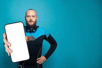 Young man diver holding smartphone with empty white screen display for new Application on blue...