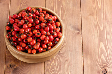 red dog-rose rosehip fruits in a wooden bowl on wooden table