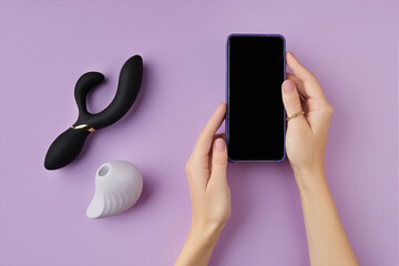 Top view of female hands holding a cellphone with adult sex toys on the purple background