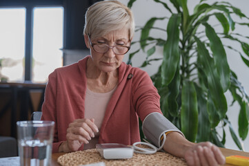 Older woman sitting alone at home, measuring her blood pressure with a home device