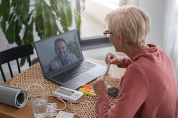 An elderly woman sitting in front of a laptop computer at home, having an online video call with a doctor. Online medical consultations. Telemedicin and telehealth
