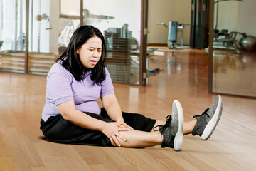 Portrait of young plus size overweight woman holding a knee suffering from osteoarthritis or...