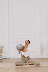 Young sports trainer-fitness instructor conducts training with a ball, isolated on a light...