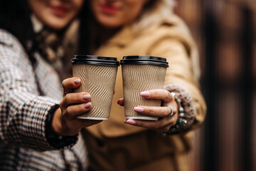 Close-up of two girls holding takeaway coffee in their hands. Picnic and going outside concept.