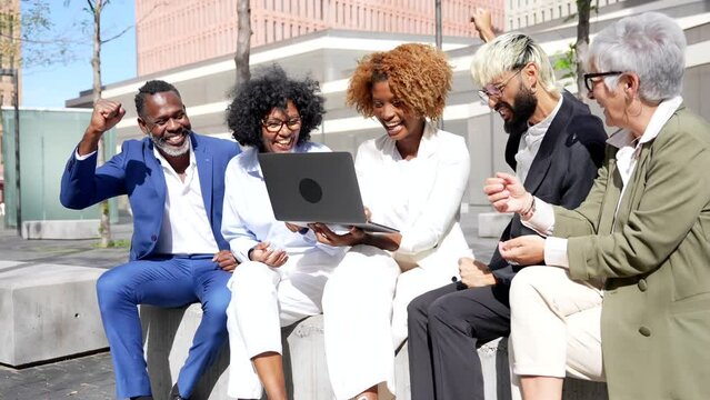 Happy group of multi-ethnic business people using laptop outdoors
