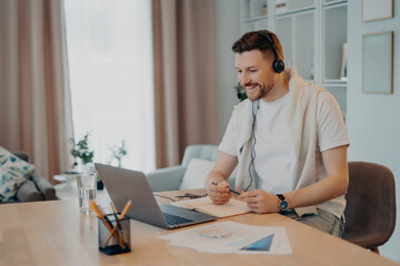 Fototapeta na wymiar Smiling young male in headset studying at home during quarantine