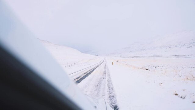 Passenger view from car driving on frozen road in winter mountains.