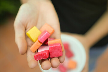 Super closeup view of yellow, red, orange and pink unhealthy candies shown by woman hand. Sugar and...