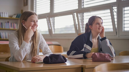 Two girl students during a classroom lecture, listening and communicating with a teacher. Education and learning concept.